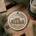 A circular ornament with the text "STONEHENGE ENGLAND" and an illustration of Stonehenge, a famous landmark in England, is displayed on a wooden surface.