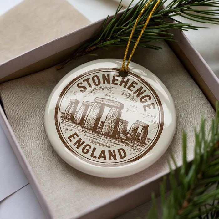A circular ornament with the text "STONEHENGE ENGLAND" printed on it, surrounded by pine branches.