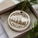 A circular ornament with the text "STONEHENGE ENGLAND" printed on it, surrounded by pine branches.