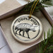 A decorative ornament featuring a striped hyena, a type of wild dog, is displayed in a box with pine branches.