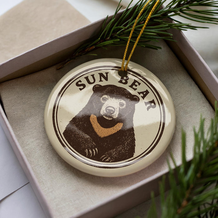 A circular ornament featuring a bear image is displayed in a box, surrounded by pine branches.