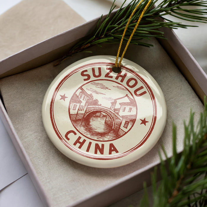 A decorative ornament in a box, featuring a circular design with the text "SUZhou China" and an illustration of a bridge.