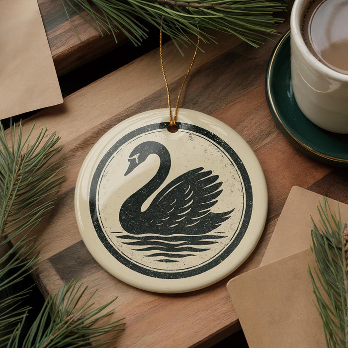 a ceramic ornament with a black and white swan design, placed on a wooden surface alongside a cup of coffee and some pine branches.