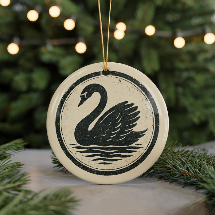A decorative ornament featuring a black swan silhouette is displayed against a blurred background of a Christmas tree with twinkling lights.