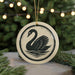 A decorative ornament featuring a black swan silhouette is displayed against a blurred background of a Christmas tree with twinkling lights.