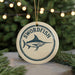 A round ornament with the word "SWORDFISH" and a graphic of a swordfish is displayed against a blurred background of a Christmas tree with lights.