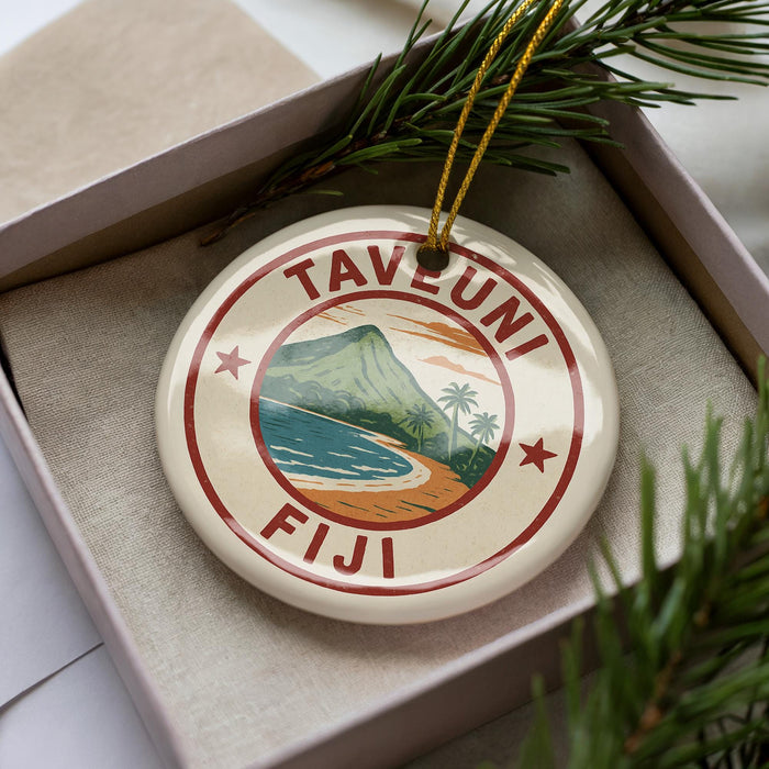 A circular ornament with the text "TAVEMUNI Fiji" and a tropical landscape design, placed in a box with pine branches.