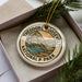 A circular ornament with the text "THEODORE ROOSEVELT NATIONAL PARK USA" printed on it, surrounded by pine branches.