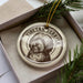 A Tibetan Terrier ornament is displayed in a box, surrounded by pine branches.