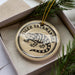 A decorative ornament in a box, featuring a black and white illustration of a salamander.