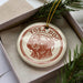 A round ornament with a dog image and the text "TOSA DOG" is displayed in a box, surrounded by pine branches.