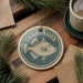 a circular ornament with a fish design, hanging on a wooden surface. The ornament has the text "TRIGGERFISH" written on it.