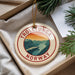 A round ornament with the text "TROLLTUNGA NORWAY" and an illustration of a mountain landscape hangs from a string.