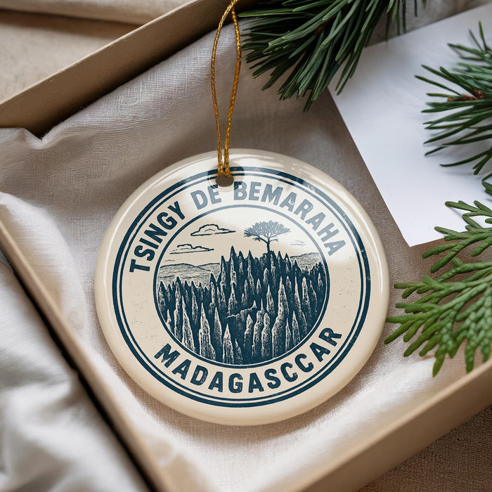 A circular ornament with a tree design and text, placed in a box with pine branches.