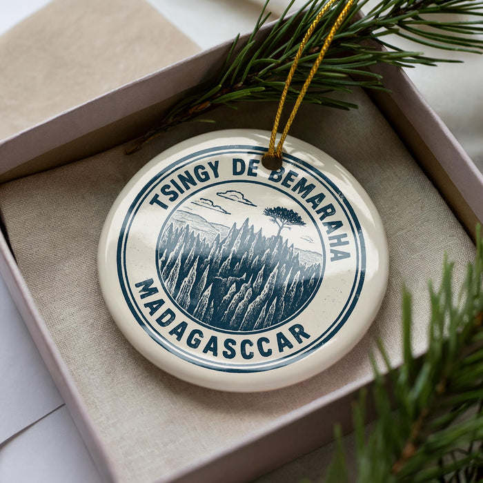 A circular ornament with a design featuring a mountain landscape and the text "TSINGY DE BEMARAH MADAGASCCAR" is displayed in a box with pine branches.