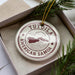 A circular ornament with the text "TUTOILA AMERICAN SAMOA" printed on it, placed inside a box with pine branches.