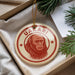 A round ornament with a red and white design featuring a monkey's face, hanging from a string.