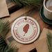 A white ceramic ornament with a red border and a map of Union Island, surrounded by pine branches and a cup of coffee on a wooden surface.
