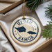 A decorative ornament with the text "UPOLU SAMOA" printed on it, featuring a map of the island of Samoa. The ornament is hanging from a string and is placed on a surface with pine branches and a white paper.