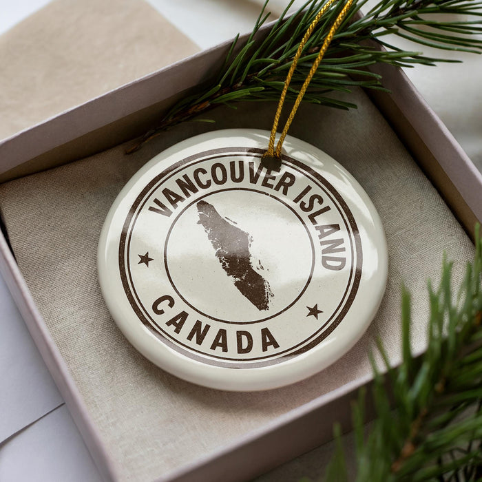 A white ornament with the text "VANCOUVER ISLAND CANADA" printed on it, surrounded by pine branches.
