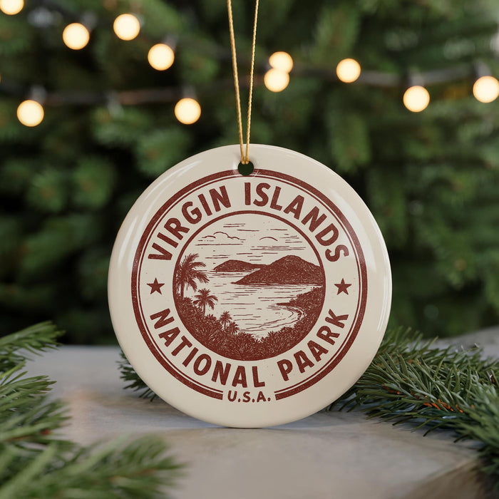 A white ornament with a red border and the text "VIRGIN ISLANDS NATIONAL PARK U.S.A." hanging from a string, placed on a surface with pine branches in the background.