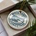 A white ceramic ornament with the text "WHITE SAND'S NATIONAL PARK USA" printed on it, placed in a box with pine branches.