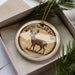 A decorative ornament in a box, featuring a deer illustration and the text "WHITE-TAILED DEER".