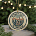 A circular ornament with a graphic of Namibia's Windhoek cityscape, featuring a church and mountains, is displayed against a blurred background of Christmas lights.