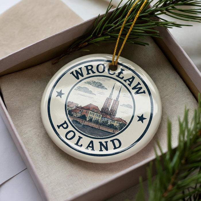 A circular ornament with the text "WROCLAW POLAND" and an illustration of a cityscape, placed in a box with pine branches.