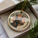 A circular ornament with a dog's head image and the text "XOLOITZCUNT" on it, placed in a box with pine branches.