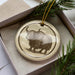 A ceramic ornament in the shape of a yak, with a brown and white color scheme, is displayed in a box with pine branches.