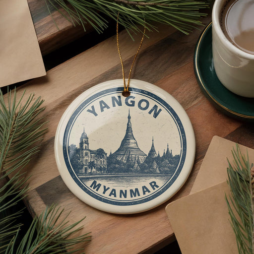 A decorative ornament featuring a temple and the text "YANGON MYANMAR" is displayed on a wooden surface, surrounded by pine branches and a cup of coffee.