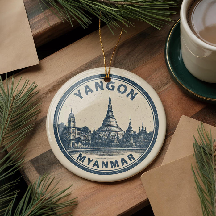 A decorative ornament featuring a temple and the text "YANGON MYANMAR" is displayed on a wooden surface, surrounded by pine branches and a cup of coffee.