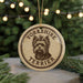 A circular ornament featuring a Yorkshire Terrier dog's head, with the text "YORKSHIRE TERRIER" printed on it, is displayed in front of a blurred Christmas tree.
