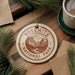 A circular ornament with the text "YOSEMITE NATIONAL PARK USA" printed on it, surrounded by pine branches and a cup of coffee on a wooden surface.