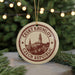 A circular ornament with a design of a town or city, surrounded by Christmas lights and greenery.