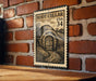 A metal sign with a vintage-style illustration of a wooden door and a path leading to a small building, mounted on a brick wall.