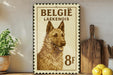 A metal sign with a picture of a dog, likely a Belgian Laekenois, is displayed on a shelf next to a wooden cutting board and some lemons.