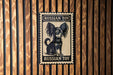 A metal sign with a black and white illustration of a dog, mounted on a wooden wall.