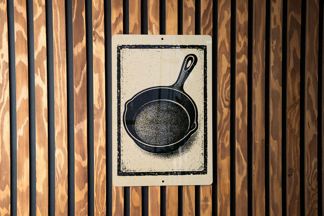 a black and white illustration of a frying pan on a wooden wall.