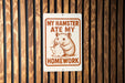 a sign with a cartoon hamster holding a piece of paper and the text "MY HAMSTER Ate MY HOMEWORK" on it.