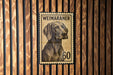 A metal stamp featuring a Weimaraner dog, with the number 60 below the dog's head.