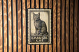 A metal sign with a cat illustration is mounted on a wooden wall.