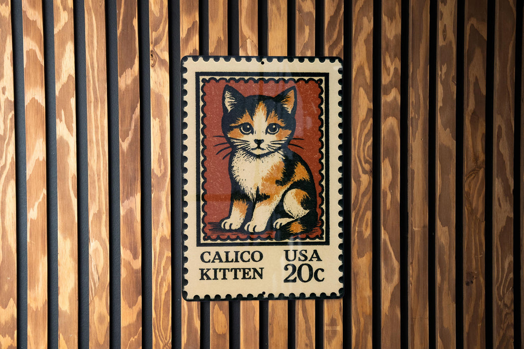 A Calico kitten postage stamp is displayed on a wooden wall.