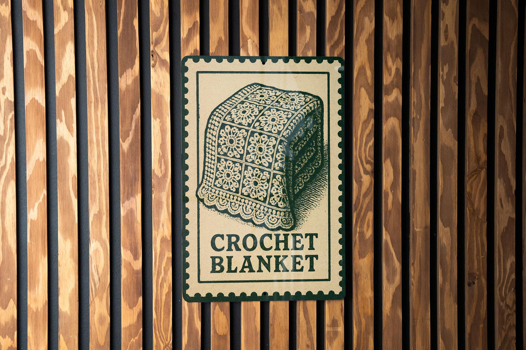 A sign with a crocheted blanket on it is displayed on a wooden wall.