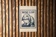 A metal sign with a rabbit illustration and the text "MINI LOP" printed on it, mounted on a wooden wall.