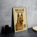 A metal sign with a dog image and text, likely a Belgian postage stamp, is displayed on a table.