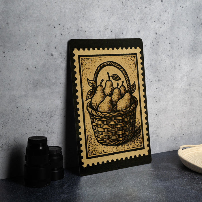 a framed illustration of a basket filled with pears, placed on a countertop next to some black camera lenses.