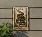 A metal sign with a snake design and the text "USA GARTER Snake" is mounted on a wall, with a plant visible to the left.