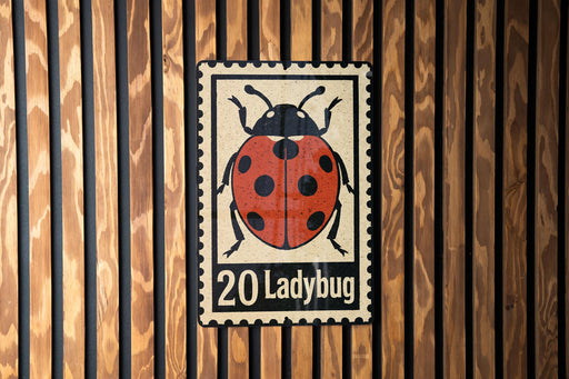 A metal sign featuring a ladybug illustration is mounted on a wooden wall.